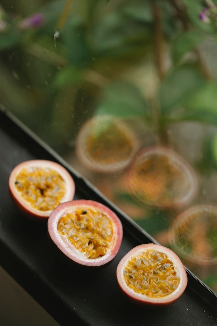 Home From above several ripe juicy appetizing halves of passion fruits placed in row on black windowsill and green plants behind glass